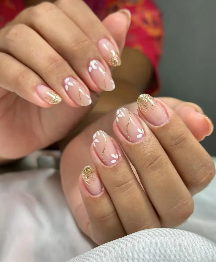Нейтральный маникюр с золотыми блестками и белыми цветами на овальных ногтях