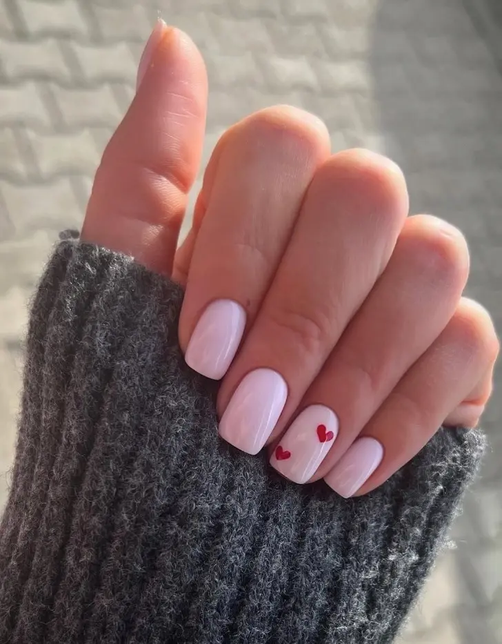 Маникюр на День святого Валентина с красными сердечками и бледно розовой основой