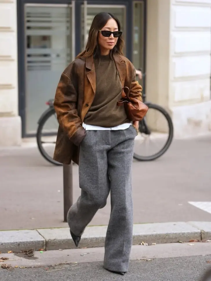 Женщина в серых брюках коричневом джемпере и кожаной куртке