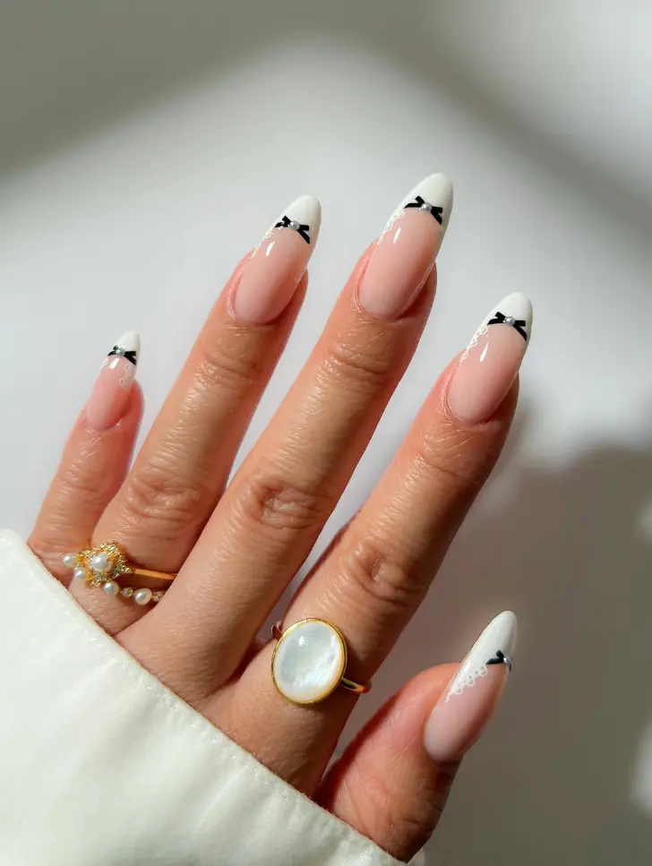 Белый французский маникюр с черными бантами на овальных ногтях